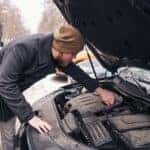 A man observing a car engine, after the car won't start on a cold winter day