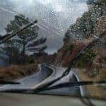 A vehicle driving through a rainy mountain road with the windshield wipers in motion.