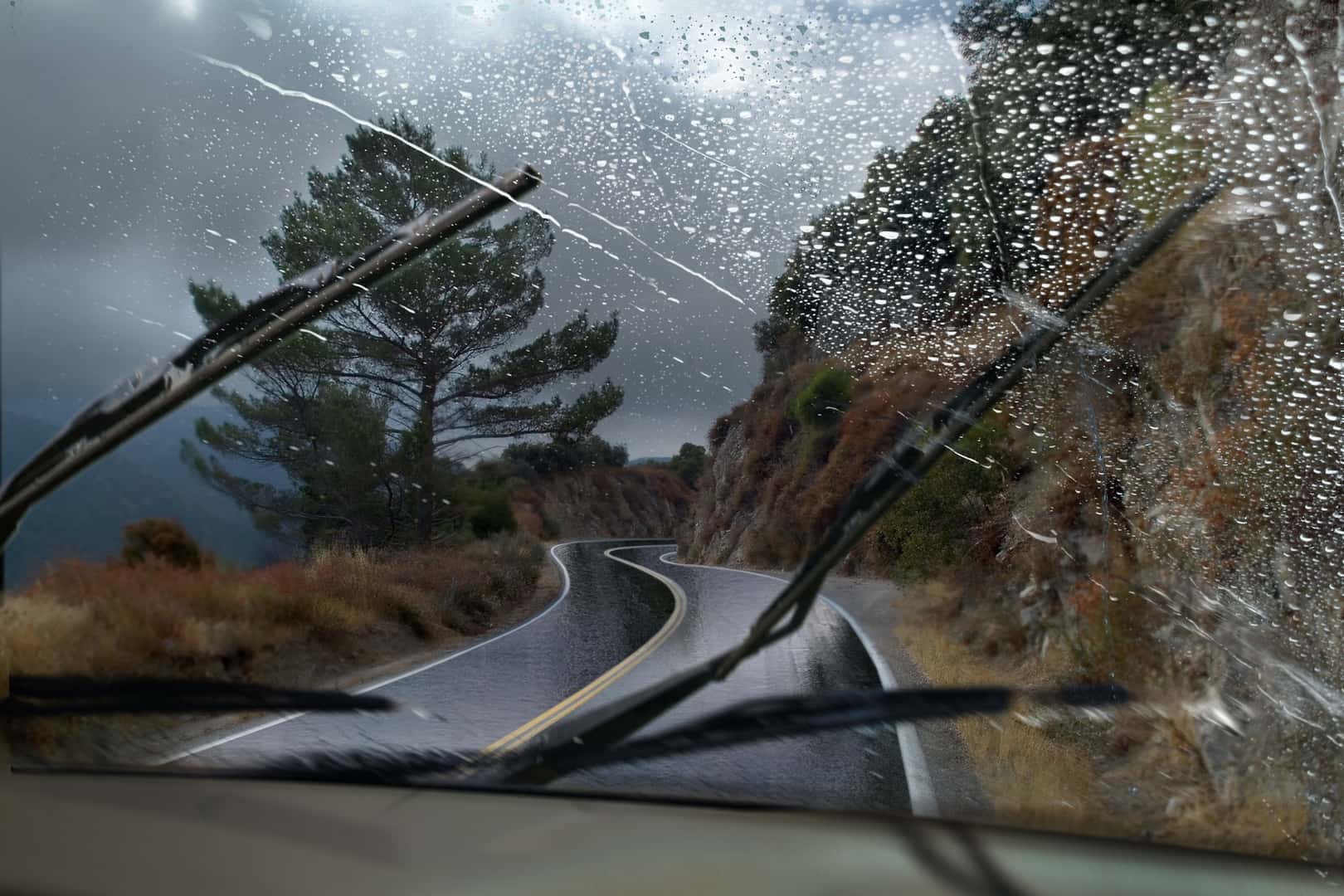 A vehicle driving through a rainy mountain road with the windshield wipers in motion.