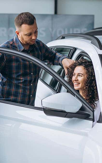 Leasing versus Buying a Toyota at CMA's Toyota of Martinsburg in Martinsburg, WV | Woman sitting happily in the passenger side of a new car while husband stand beside her