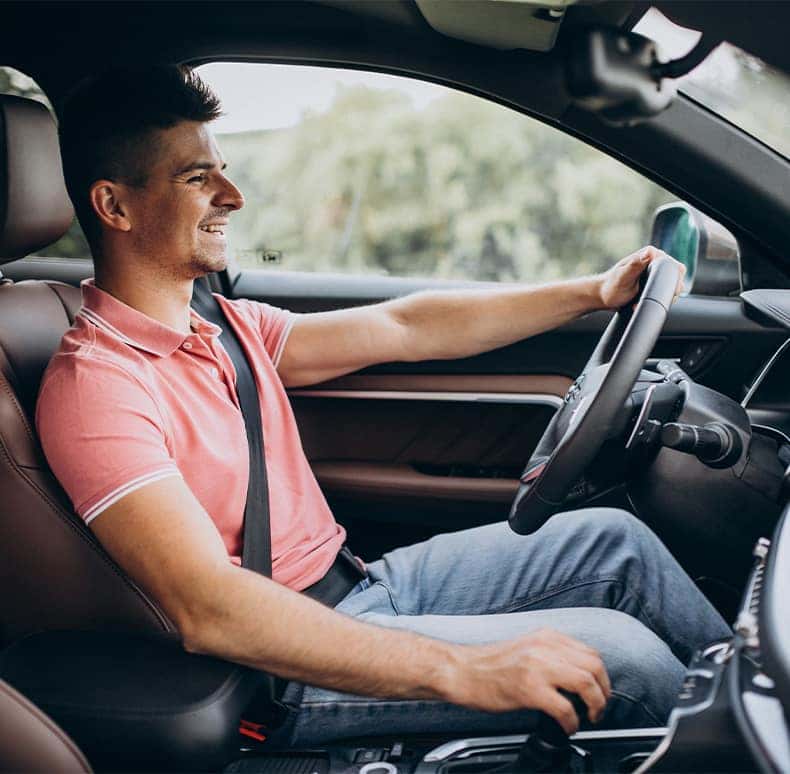 Enjoy A Test Drive At  CMA's Toyota of Martinsburg in Martinsburg, WV | Man in pink polo shirt is happy driving his car with his hand on the steering wheel