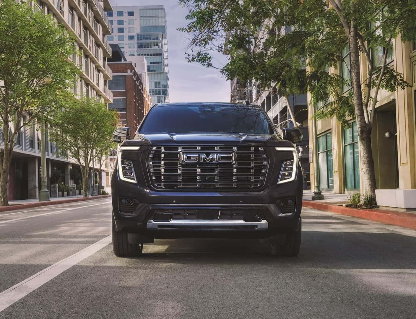 Blue GMC Yukon driving on road with buildings on either side