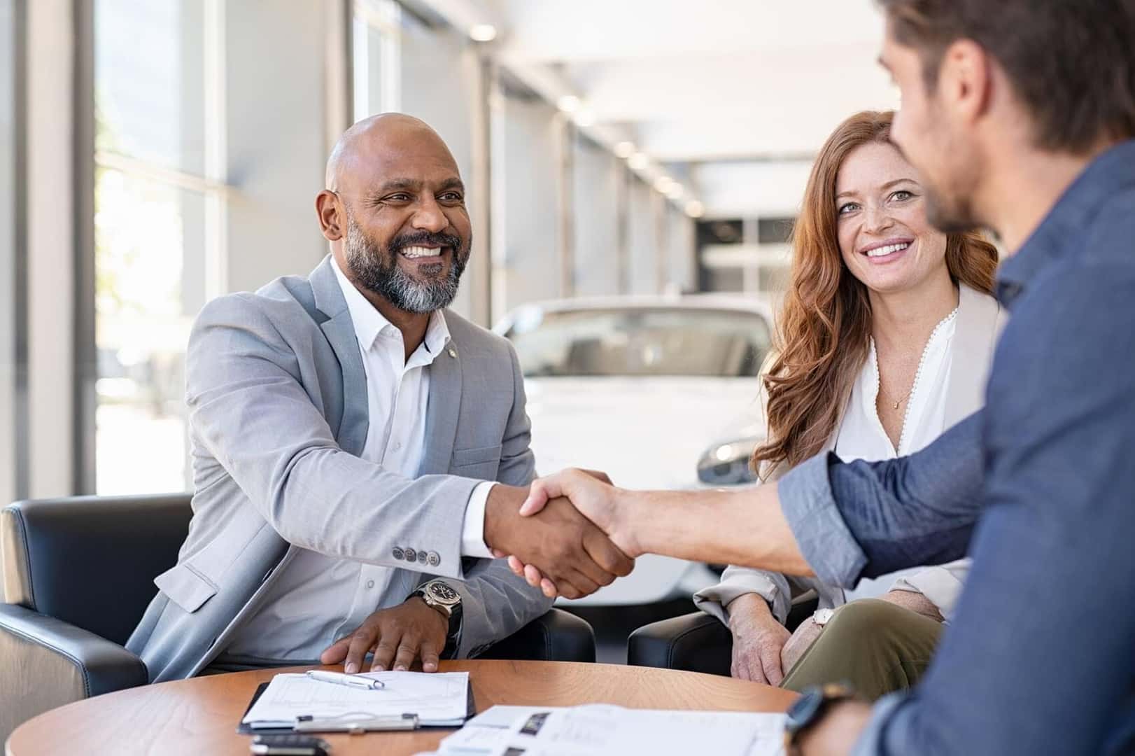 Dealershio sales man shaking hands with couple purchasing car