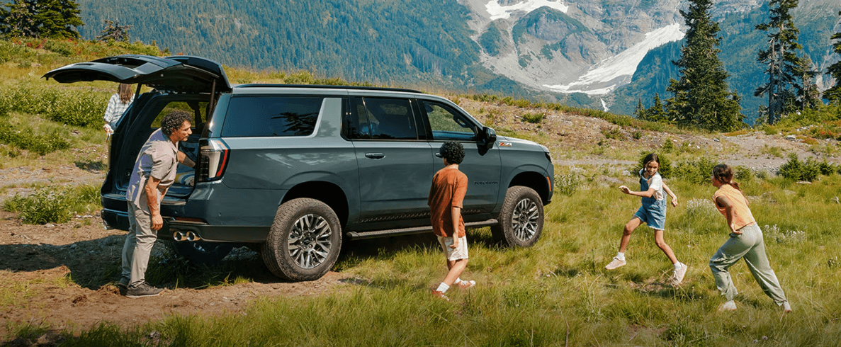 Family unloading a 2026 Chevrolet Suburban in a grassy mountain landscape