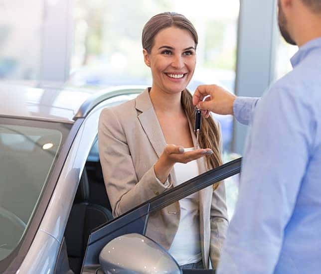 salesman handing keys to woman who is standing between drivers door of silver car