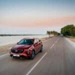 A red Cadillac XT4 being driven on a road along a lake.