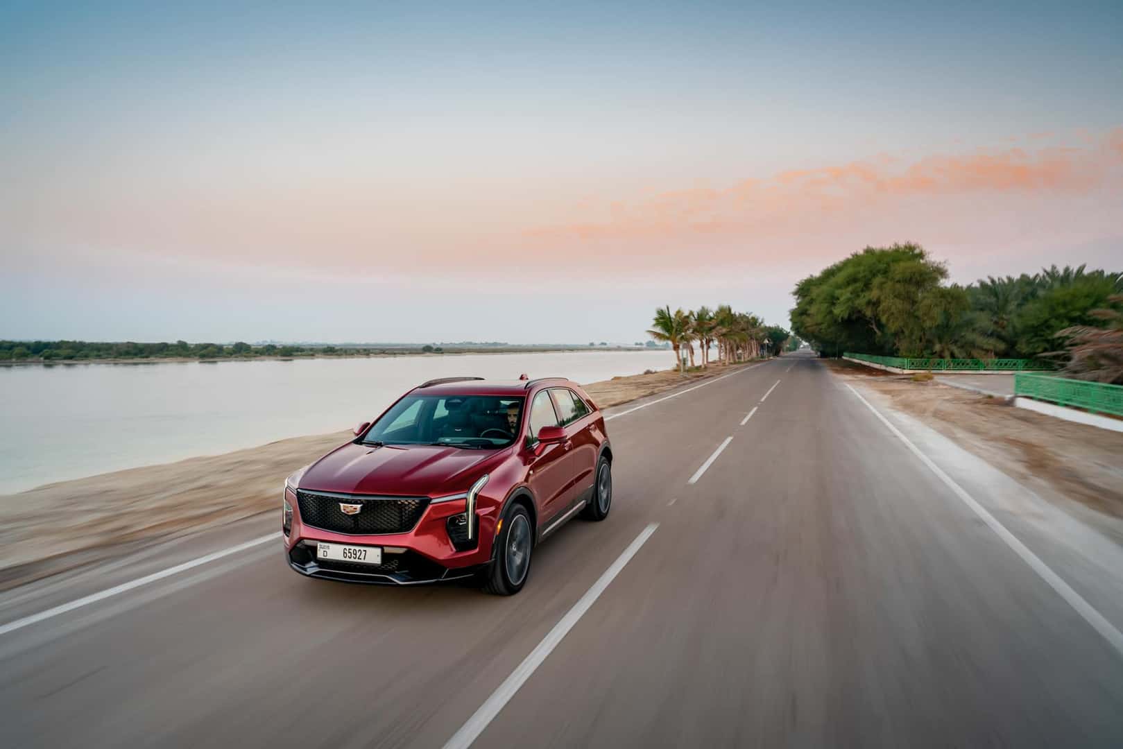A red Cadillac XT4 being driven on a road along a lake.