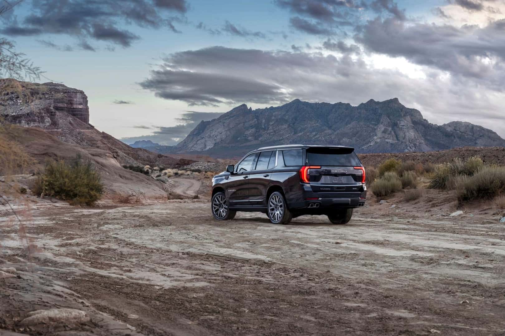 The Powerful Back Profile Of The 2025 GMC Yukon Denali Ultimate, Driving In The Desert Under Cloudy Skies
