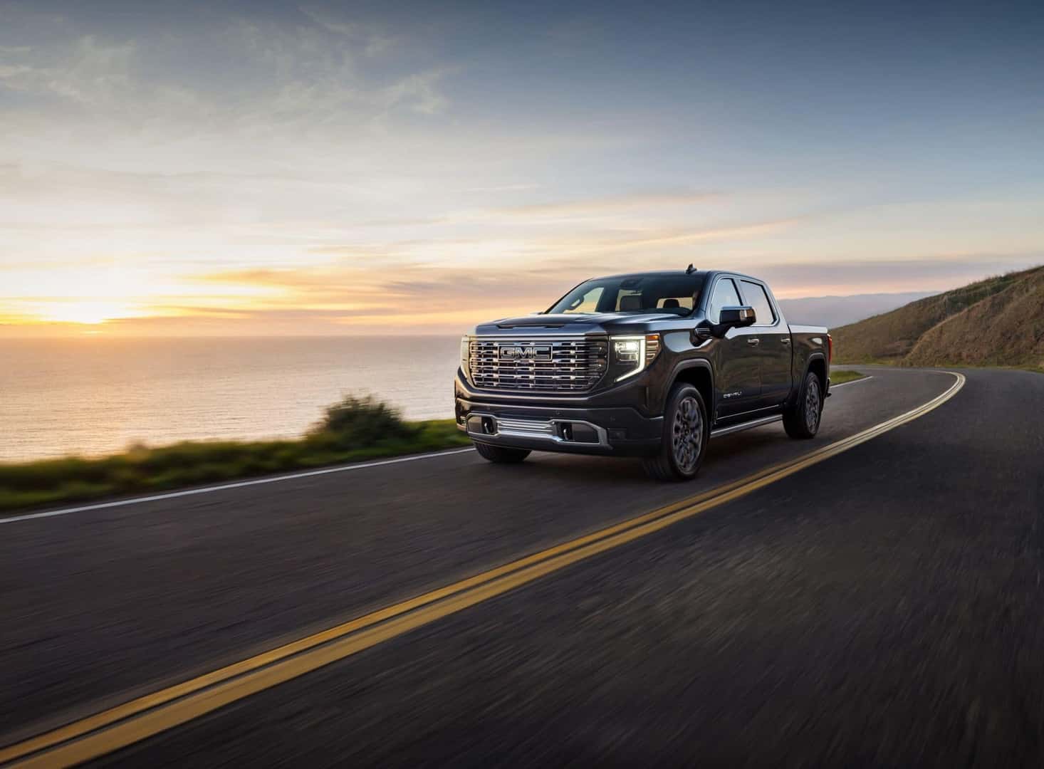 A Bold Black 2024 GMC Sierra Denali Speeding On The Highway In The Eyes Of The Sunset