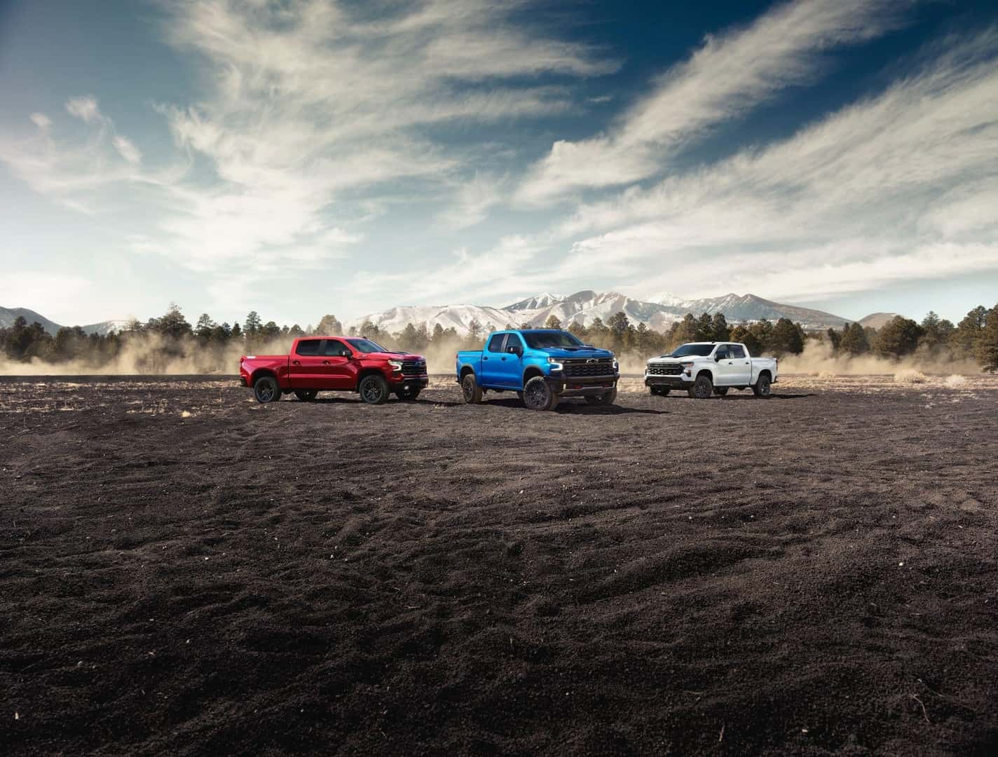 The Epic 2025 Chevrolet Silverado Lineup, Parked Gloriously On Dark Sand, With Foggy Trees And High Mountains In The Beautiful Background