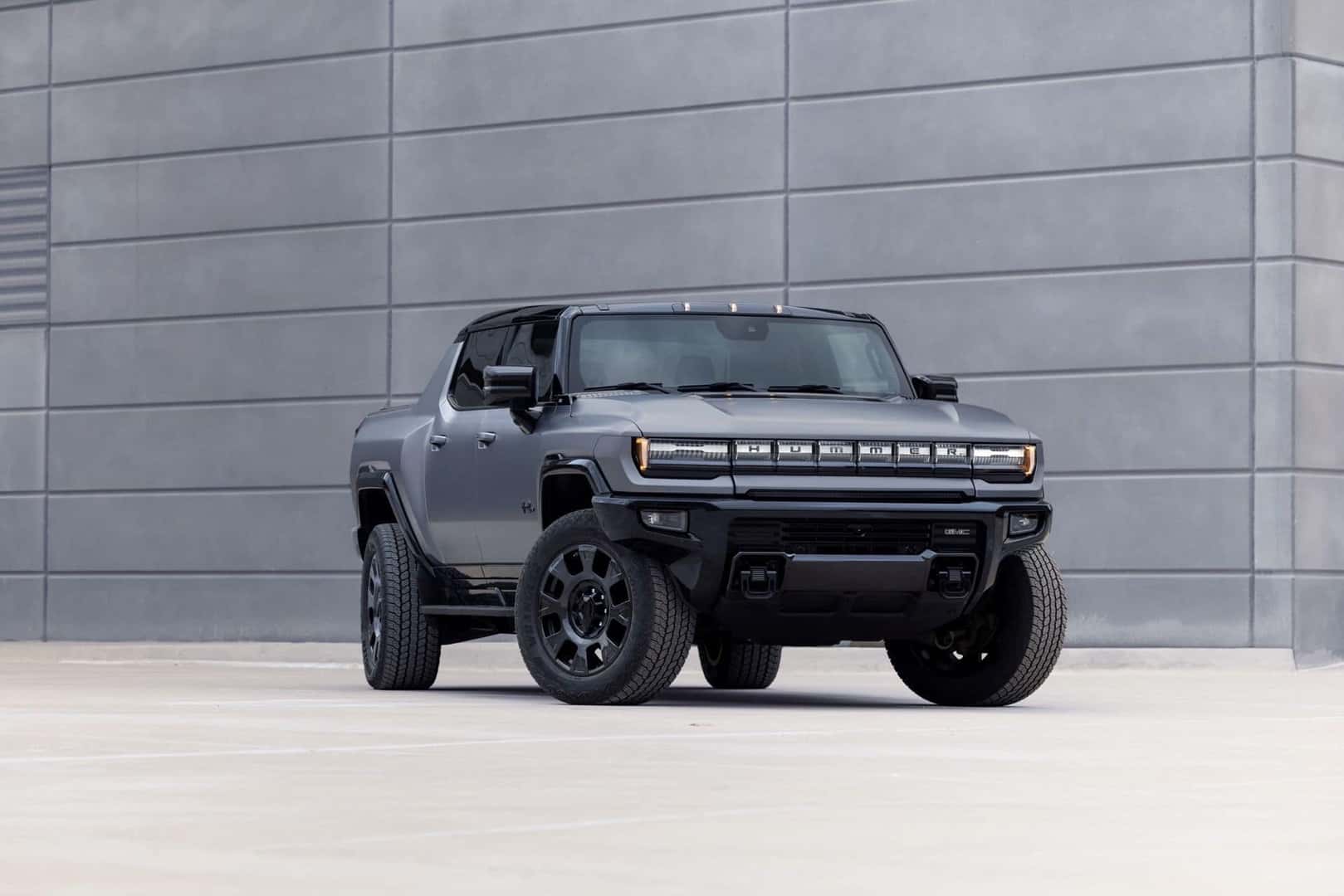 A Grey-Colored 2026 Hummer EV Parked In Front Of A Stone Wall