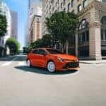 An Orange 2026 Corolla Hatchback FX Turning Gracefully At An Elegant City Intersection