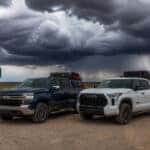 2026 Chevrolet Silverado 1500 and 2026 Toyota Tundra parked on a South Dakota prairie road with storm clouds overhead