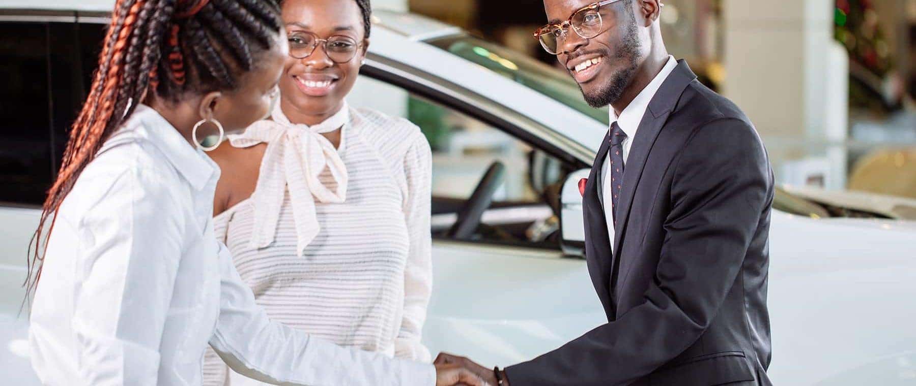 couple shaking hands with car saleswoman
