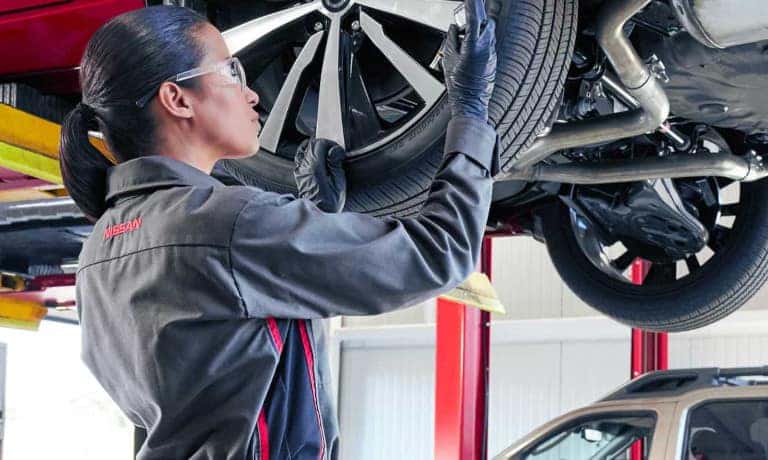 Nissan Service Technician Working On Tire With Gauge