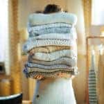 woman in modern house in sunny winter day holding huge sweaters