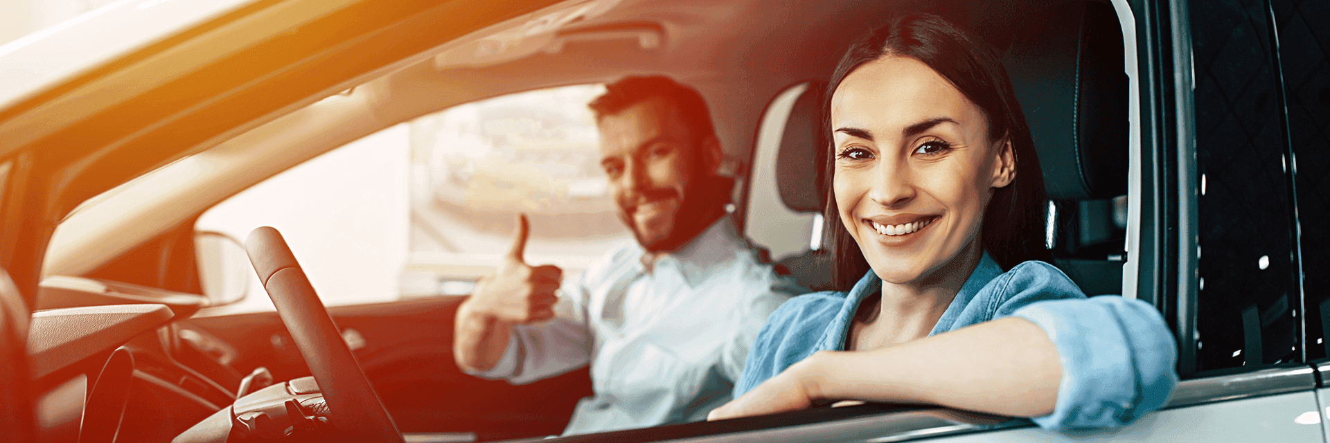 A smiling couple sitting in a car giving a thumbs up