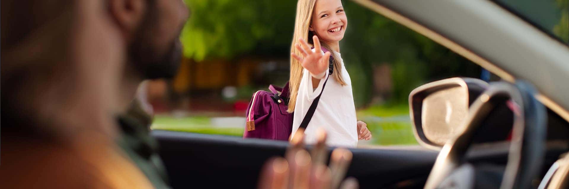 small child with backpack waving to parents in car