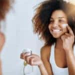 Shot of a woman applying moisturizer to her face in front of the mirror
