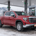 GMC Sierra 1500 with 3.0L Duramax diesel fueling at a Northern Colorado station in winter with snow-dusted Rocky Mountain foothills in the background