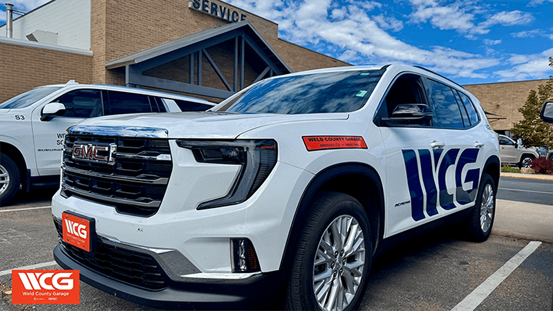 A Weld County Garage courtesy shuttle, a white GMC Acadia, parked outside the Greeley service entrance