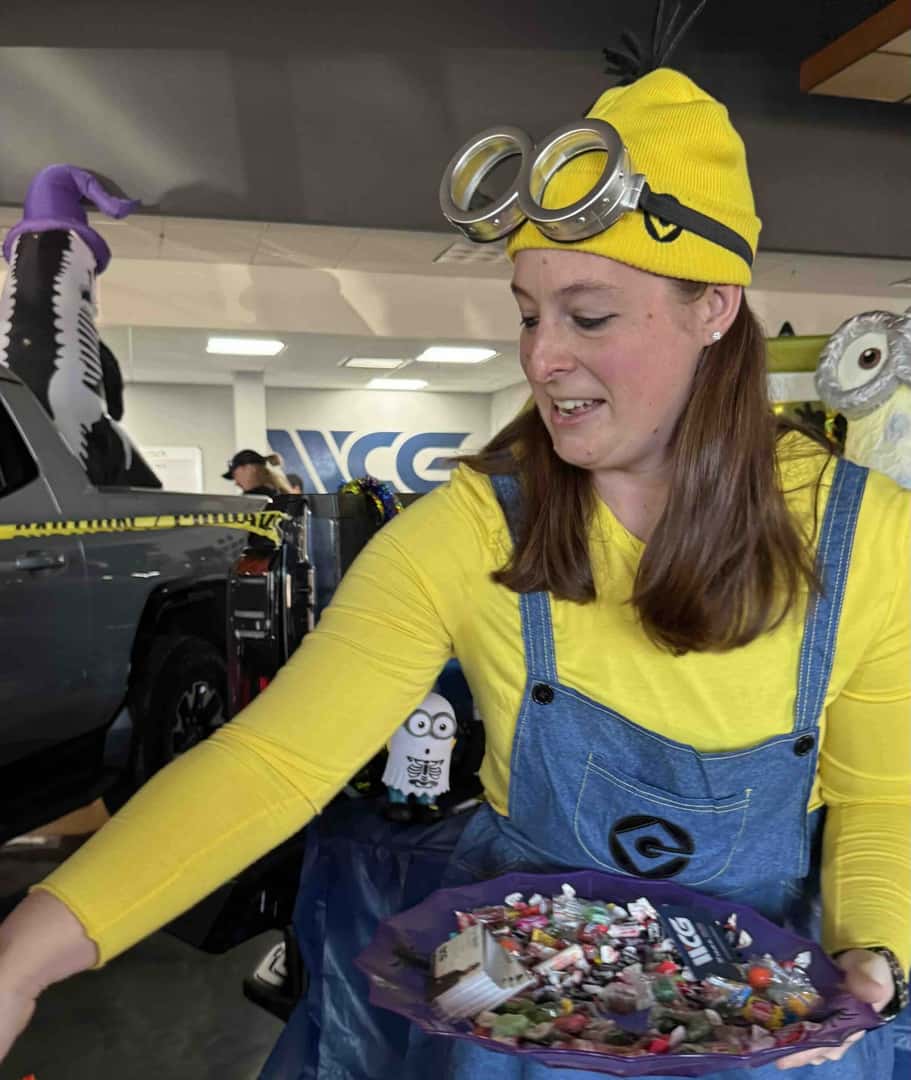 A Weld County Garage team member in a yellow and blue costume hands out candy from a full bowl at Trunk or Treat.